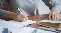 Una persona tomas notas en un cuaderno mientras hojea un libro