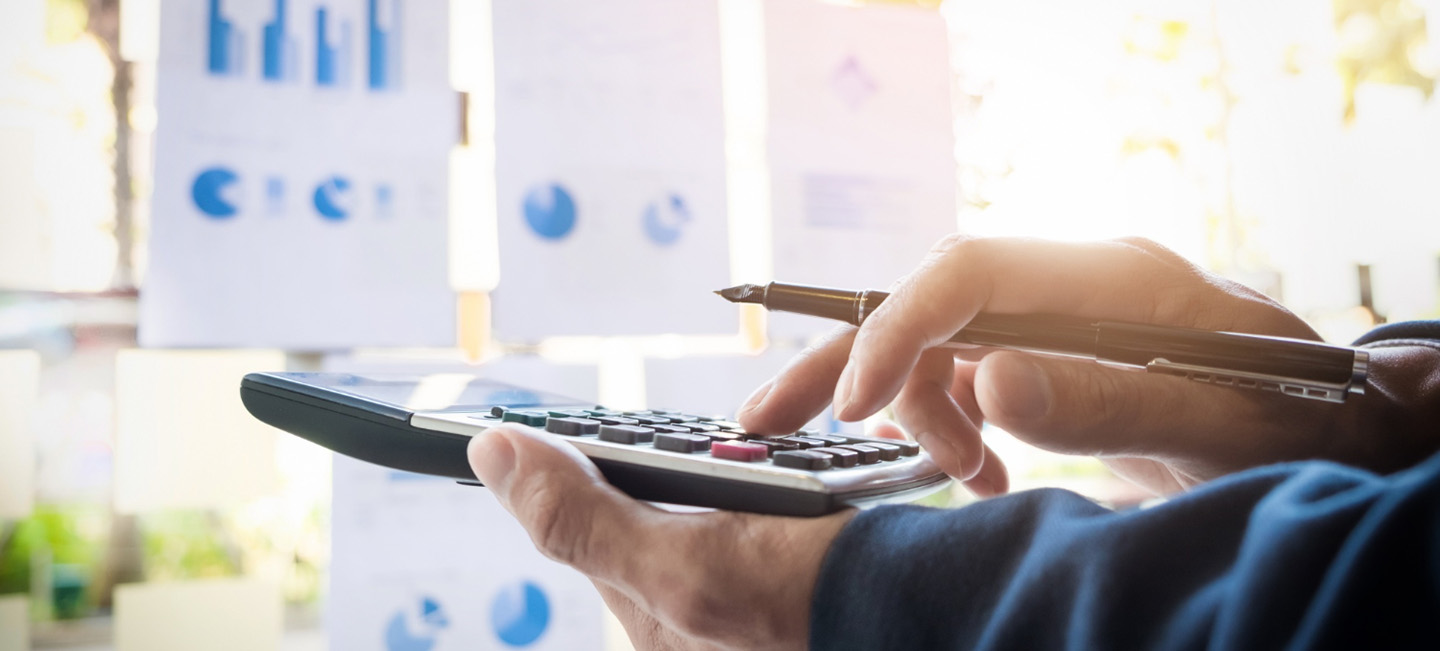 Una persona hace operaciones con una calculadora frente a unos gráficos