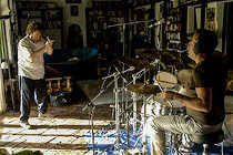 Un hombre toca las palmas y otro la batería en un estudio