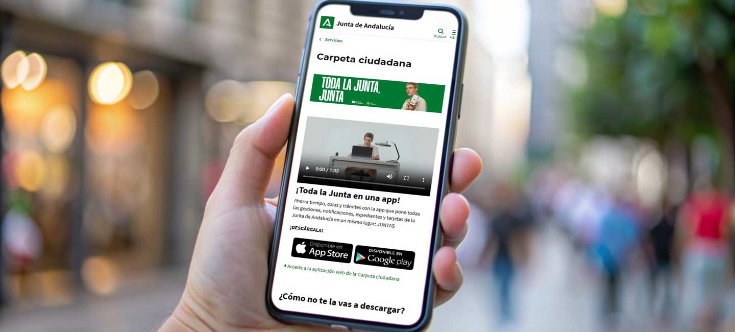 Una mano sostiene un teléfono móvil en cuya pantalla aparece la web de carperta ciudadana