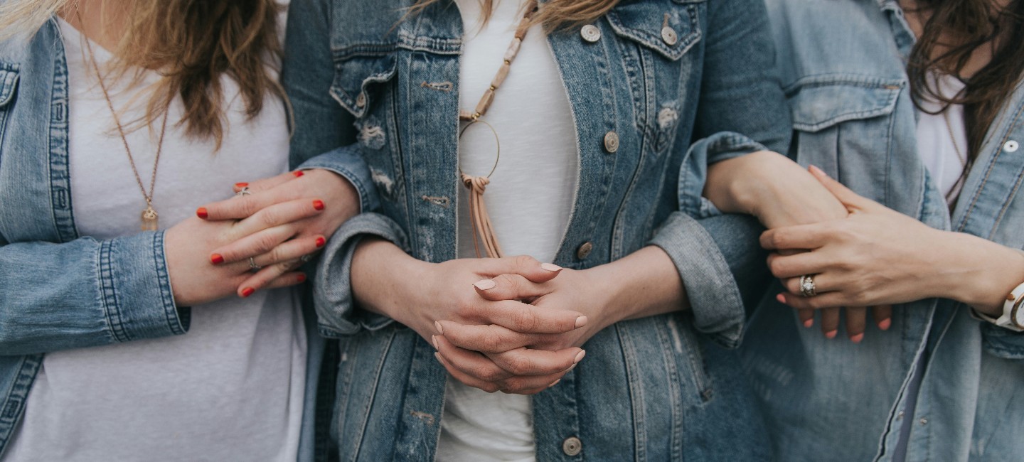 Tres mujeres entrelazan sus brazos y cada una de ellas une sus manos